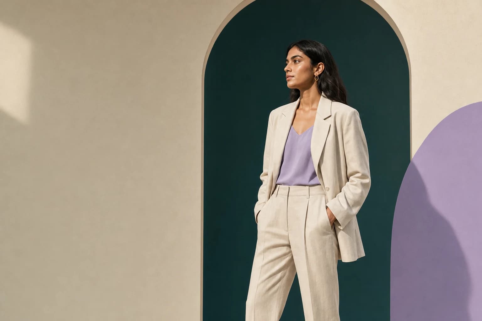 Woman in an ivory blazer and lavender top standing in a deep teal arch